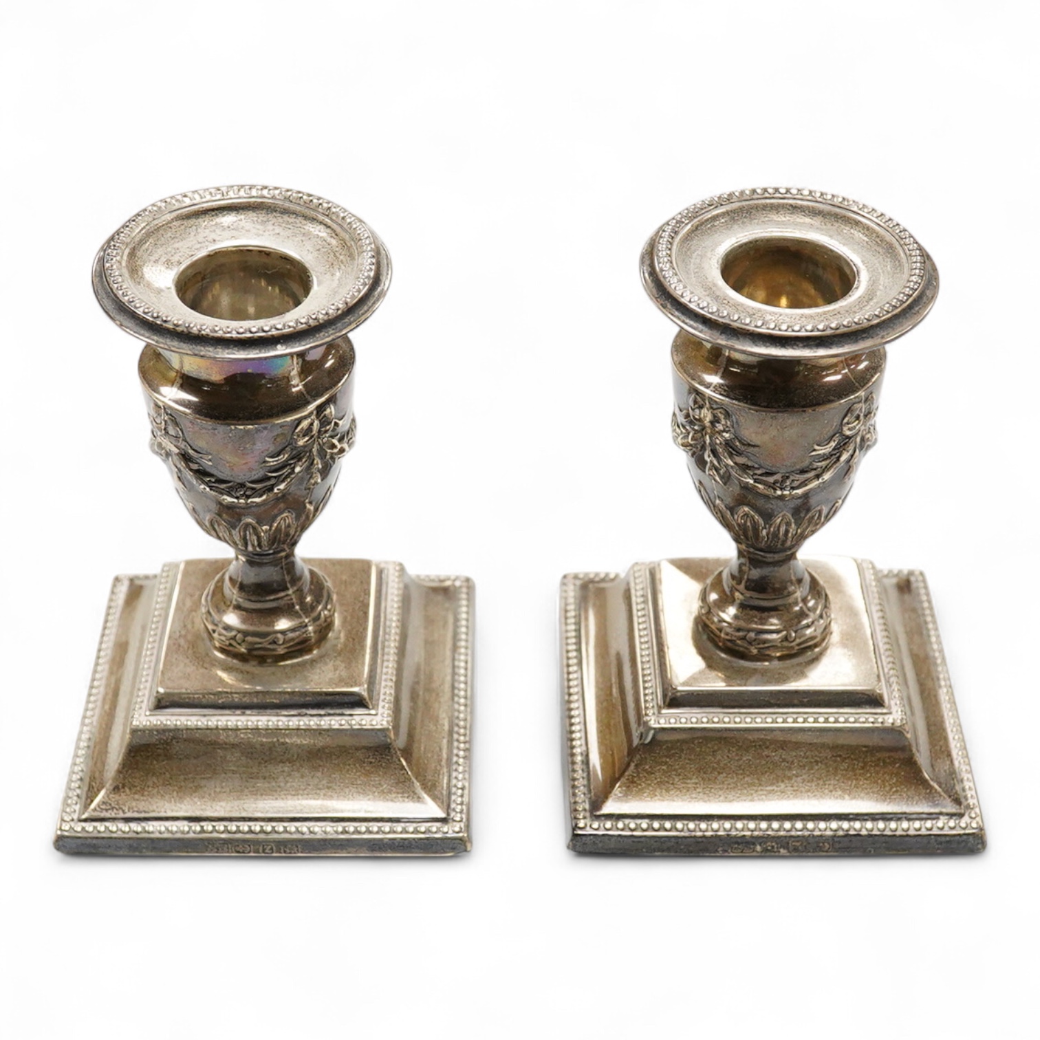 A pair of late Victorian silver mounted dwarf candlesticks, embossed with swags, on beaded bases, by Barker Brothers, Birmingham, 1899, height 11.5cm, weighted.